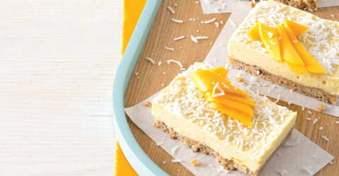 Stack of square Mango Coconut Bliss Bars on a plate with fresh mango slices. 